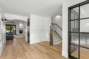 Unfurnished living room featuring a glass covered fireplace, light wood-style floors, ceiling fan, a decorative wall, and stairway