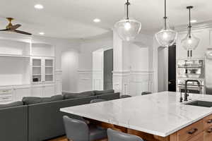 Kitchen with a breakfast bar, ornamental molding, a center island with sink, light stone counters, and open floor plan