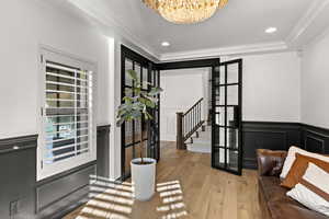 Entrance foyer featuring a chandelier, light wood-style floors, stairs, crown molding, and a decorative wall