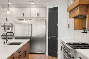 Kitchen with brown cabinets, white cabinetry, high quality appliances, light stone countertops, and pendant lighting