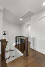 Stairs featuring arched walkways, recessed lighting, wood finished floors, and a textured ceiling
