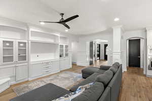 Living room with crown molding, light wood-style floors, arched walkways, a ceiling fan, and a decorative wall