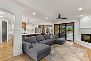 Living room featuring ornamental molding, light wood finished floors, arched walkways, a glass covered fireplace, and recessed lighting