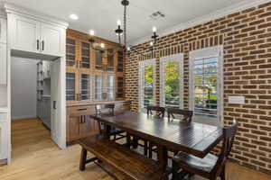 Dining area featuring brick wall, light wood-style floors, a chandelier, crown molding, and recessed lighting
