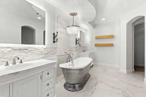 Full bath with a freestanding tub, two vanities, light marble finish floors, recessed lighting, and backsplash