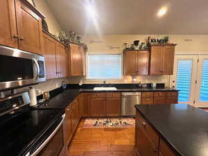 Kitchen with stainless steel appliances, hardwood cabinets and floors and black Corian countertops.