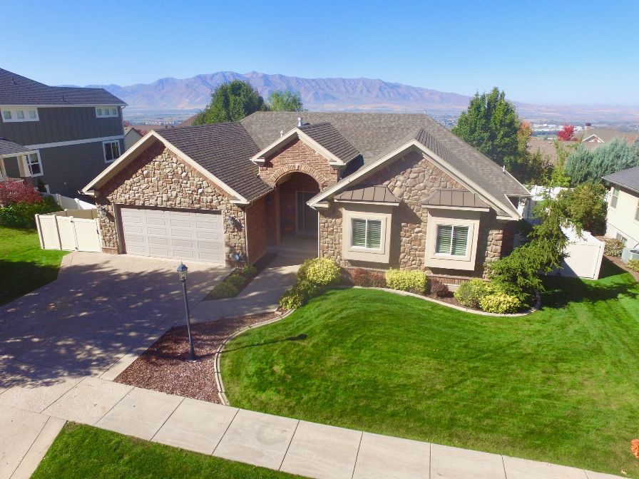 View of front facade with stone siding, driveway, a mountain view, an attached garage, and a standing seam roof.