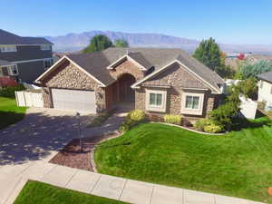 View of front facade with stone siding, driveway, a mountain view, an attached garage, and a standing seam roof.