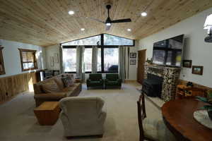 Carpeted living area with a wainscoted wall, wooden walls, vaulted ceiling, wood ceiling, and a wood stove