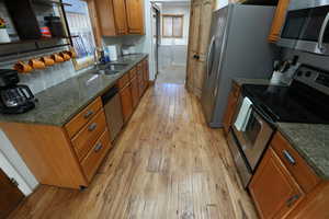 Kitchen with stainless steel appliances, dark stone counters, washer and clothes dryer, light wood-style flooring, and brown cabinets