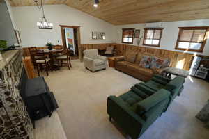 Living area featuring wooden walls, wood ceiling, wainscoting, vaulted ceiling, and light carpet