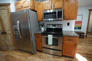 Kitchen featuring appliances with stainless steel finishes, light wood finished floors, and dark stone countertops
