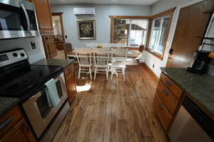 Kitchen with stainless steel appliances, brown cabinetry, dark wood-type flooring, dark stone countertops, and a wall mounted AC