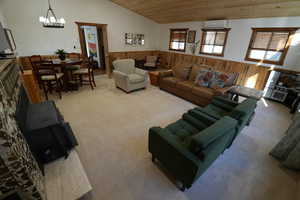 Carpeted living room featuring wooden walls, wainscoting, vaulted ceiling, wooden ceiling, and a chandelier