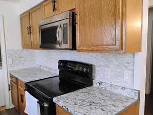 Kitchen featuring black electric range oven, stainless steel microwave, light countertops, and decorative backsplash