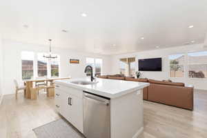 Kitchen featuring stainless steel dishwasher, light wood-type flooring, pendant lighting, white cabinetry, and healthy amount of natural light