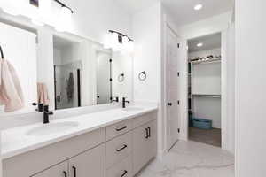 Full bath featuring double vanity, light marble finish flooring, a marble finish shower, recessed lighting, and a walk in closet