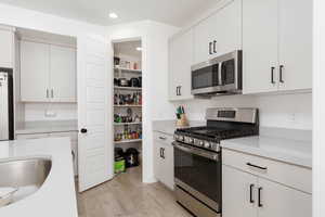Kitchen with appliances with stainless steel finishes, light wood-type flooring, white cabinetry, and recessed lighting