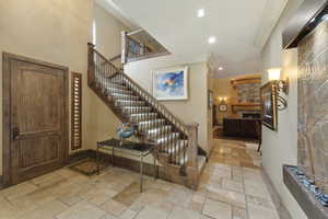 Foyer with ornamental molding, stone tile floors, stairway, a high ceiling, and a stone fireplace