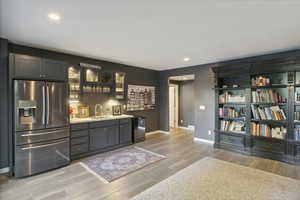 Bar area featuring stainless steel fridge with ice dispenser, recessed lighting, glass insert cabinets, light wood finished floors, and gray cabinets