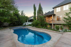 Pool at dusk with a balcony and a fenced backyard