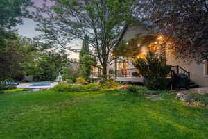 Yard at dusk featuring a wooden deck, a yard, and an outdoor pool