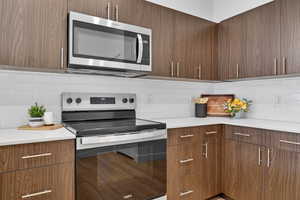 Kitchen featuring dark wood finish cabinets, a peninsula, modern cabinets, stainless steel appliances, and decorative pendent lights.