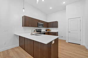 Kitchen featuring dark wood finish cabinets, a peninsula, modern cabinets, stainless steel appliances, and decorative pendent lights.