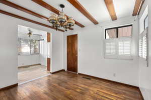 Unfurnished room featuring a chandelier, dark wood finished floors, beamed ceiling, and ceiling fan