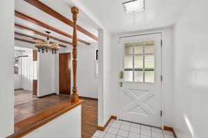 Doorway to outside featuring beam ceiling, a chandelier, wood finished floors, and a textured ceiling