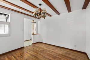 Empty room featuring a chandelier, beamed ceiling, and wood finished floors