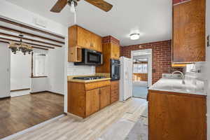 Kitchen with ceiling fan, light countertops, beamed ceiling, brown cabinets, and light wood finished floors