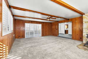 Unfurnished living room featuring wood walls, beamed ceiling, carpet flooring, and ceiling fan
