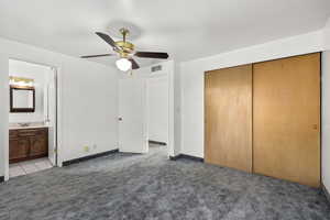 Unfurnished bedroom featuring dark carpet, a closet, ceiling fan, and connected bathroom