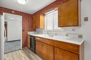 Kitchen with brick wall, light wood finished floors, brown cabinets, freestanding refrigerator, and dishwasher