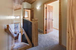 Hallway with an upstairs landing, carpet flooring, vaulted ceiling, and wood ceiling