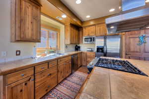 Kitchen with extractor fan, brown cabinets, stainless steel appliances, recessed lighting, and tile counters