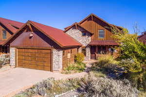 View of front of property with stone siding, an attached garage, driveway, and a porch