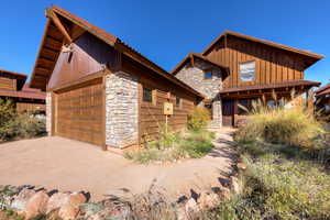 View of front of home with stone siding, a garage, board and batten siding, and an outdoor structure