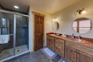 Bathroom featuring double vanity, dark tile patterned floors, and a shower stall
