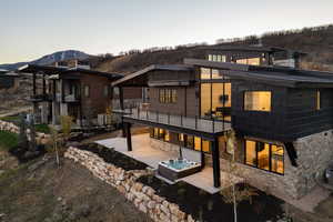 Back of property at dusk featuring a hot tub, a patio area, a mountain view, stone siding, and a balcony