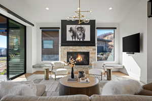 Living area featuring wood finished floors, a stone fireplace, recessed lighting, and a chandelier