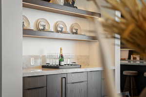 Bar area featuring modern cabinets, open shelves, gray cabinets, and light stone counters