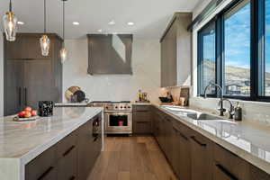 Kitchen with light stone counters, premium stove, light wood-style flooring, decorative backsplash, and wall chimney range hood