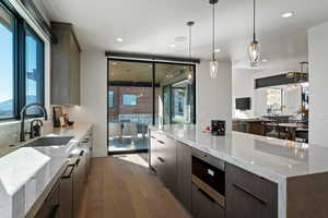Kitchen featuring light stone counters, light wood finished floors, modern cabinets, stainless steel microwave, and pendant lighting
