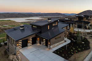 Contemporary home featuring a chimney, a standing seam roof, concrete driveway, and stone siding