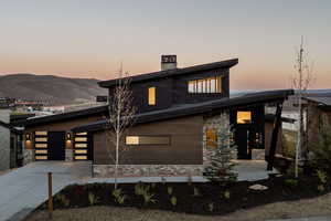 View of front of house featuring stone siding, a chimney, concrete driveway, and a garage