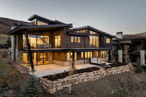 Rear view of house with a balcony, stone siding, a patio area, and a chimney