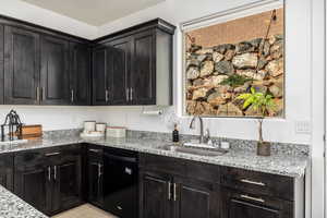 Kitchen with light stone countertops, dishwasher, and dark cabinetry