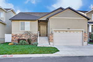 View of front of home with stone siding, an attached garage, stucco siding, concrete driveway, and a front yard